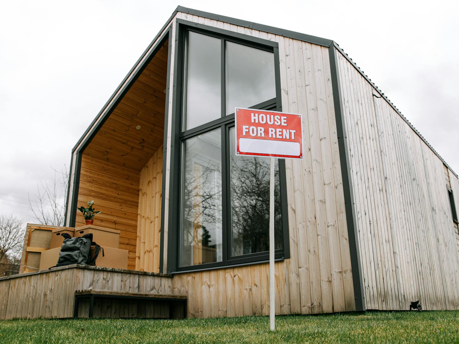 Low-angle view of a modern wooden house with a 'House for Rent' sign, showcasing contemporary architecture, renters.